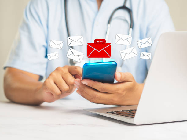 istock Doctor using a mobile receives a new message with unread email icons while sitting at a desk. 1989221997