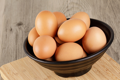 Close up of a bowl of fresh raw Brown Eggs with a wooden background and copy space