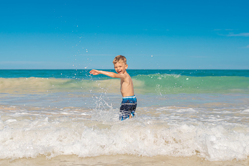 Happy little boy playing in the ocean. Summer beach vacation.