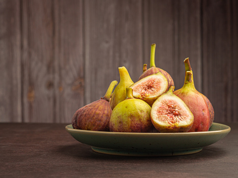 A pile of ripe fig fruits is on a plate with a wooden background. High-vitamin fruit. Close-up photo. Healthy fruits and healthcare concepts.