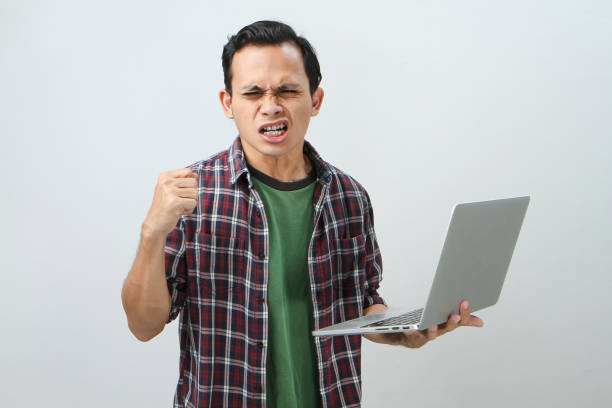 Angry mad asian indonesian man holding laptop computer on isolated background