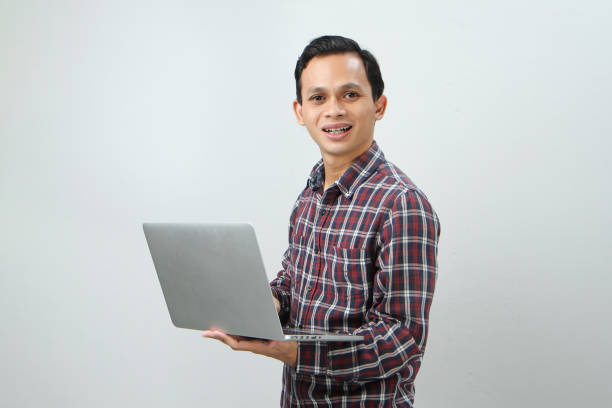 istock Happy asian indonesian man holding laptop computer on isolated background 1989230965