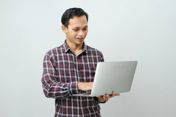 istock Happy asian indonesian man holding laptop computer on isolated background 1989231869