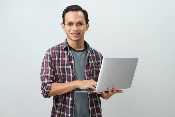 istock Happy asian indonesian man holding laptop computer on isolated background 1989234449