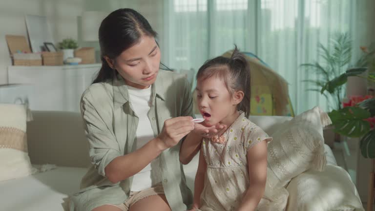 Mom takes Care of her daughter who gets sick and has a high fever, cold, and flu, and feeds medicine to her child at home. Illness Girl with a medical condition and family wellness.