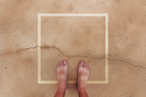 Barefoot male standing on wet concrete surface with square frame as copy space, top view pov image