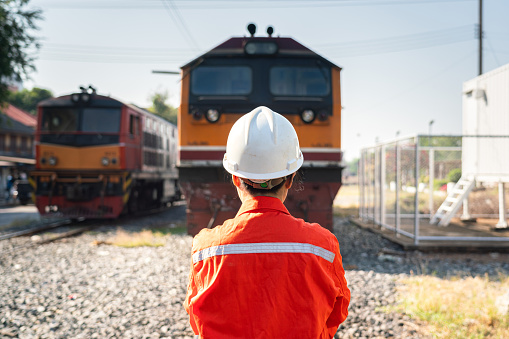 Back from a female engineer in orange working uniform with white safety helmet is standing on crude oil and chemical freight cargo train. Ready to working in challenge logistic industrial concept.
