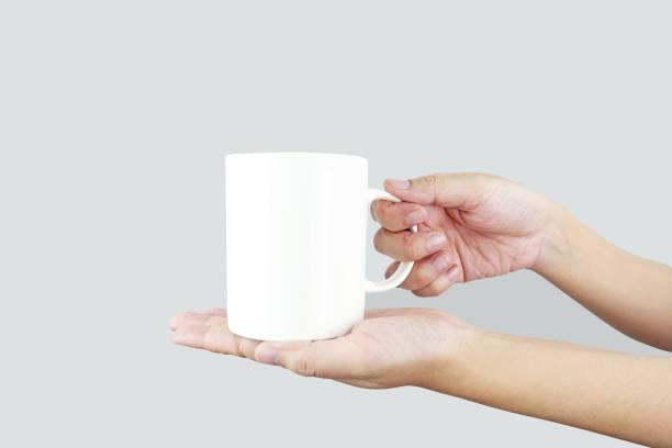 istock Hands holding a mockup of a white empty mug on a gray background,  for your logo design. 1989350206