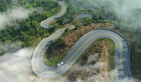 Aerial view of dark green forest road and white electric car Natural landscape and elevated roads Adventure travel and transportation and environmental protection concept