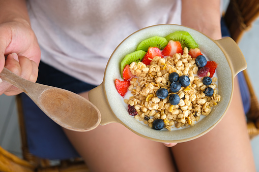 Woman's hands holding a yogurt bowl with blueberries, kiwi, strawberries and granola  healthy food and weight control concept.