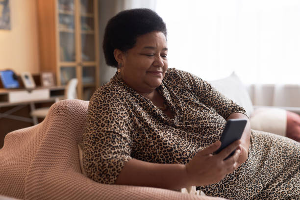 istock Black Senior Woman Using Phone Relaxing on Couch in Cozy Home 1989444372