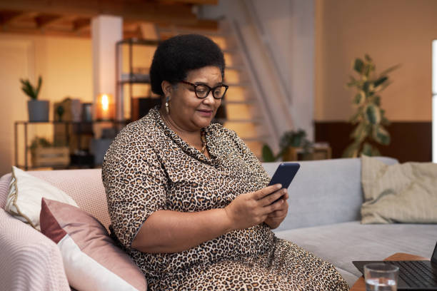 istock Black Senior Woman Using Phone Sitting on Sofa 1989444387
