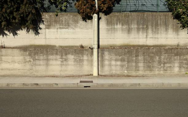 istock Cement pole on sidewalk with precast concrete wall on behind. Branches of tree on top, urban street in front. 1989449142