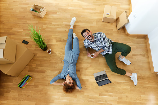 High angle view of cheerful couple talking while relaxing on the floor during a break from unpacking their belongings in new apartment. Copy space.