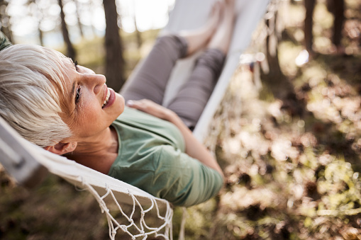 Happy mature woman day dreaming while relaxing in hammock at the backyard.