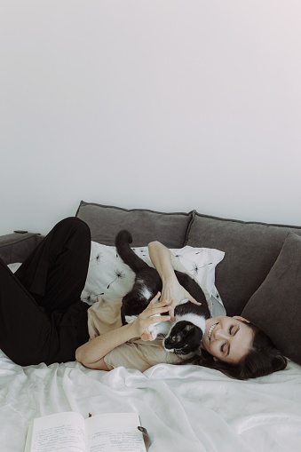 Cats friendly. Attractive young woman playing with her cat and smiling while lying in bed at home. Photo with place for text.