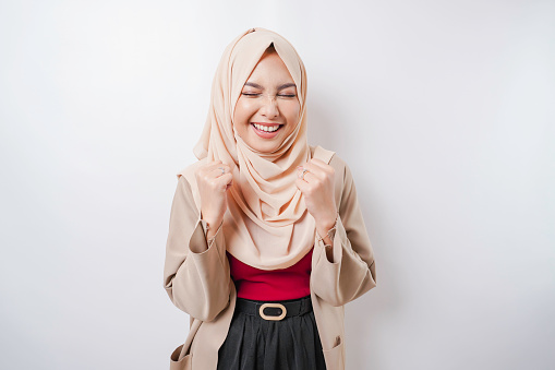 A young Asian Muslim woman with a happy successful expression wearing a hijab isolated by white background