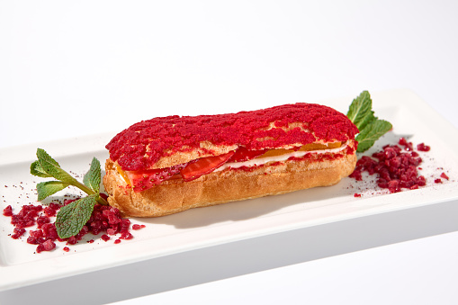 Raspberry eclair on an isolated white background, elegantly presented with a dusting of red powder.