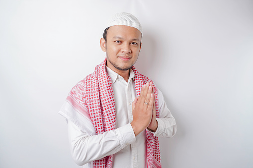 Smiling young Asian Muslim man, gesturing traditional greeting isolated over white background