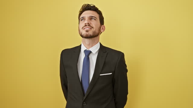 Cheerful young hispanic man confidently smiling, dressed in a business suit. natural relaxed pose, standing sideways isolated on a yellow background