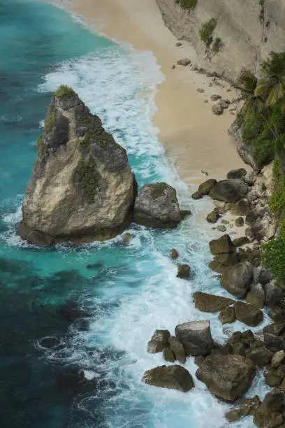 Scenic rugged coastline of sea stacks rocks, white sand beach and breaking waves  on a tropical Nusa Penida island