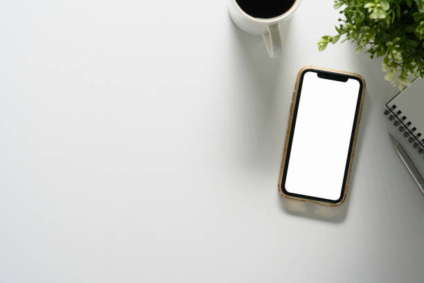 istock Top view smartphone with blank screen, coffee cup, notepad and house plant on white table, copy space 1989588154
