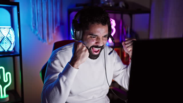 Excited man with beard celebrating success while gaming at home at night.