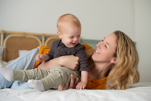 Mom, baby and family home with love, support and care with a smile in a bedroom. Happy, mother and young boy together in the morning with bonding, youth and bed in a house with childhood and fun