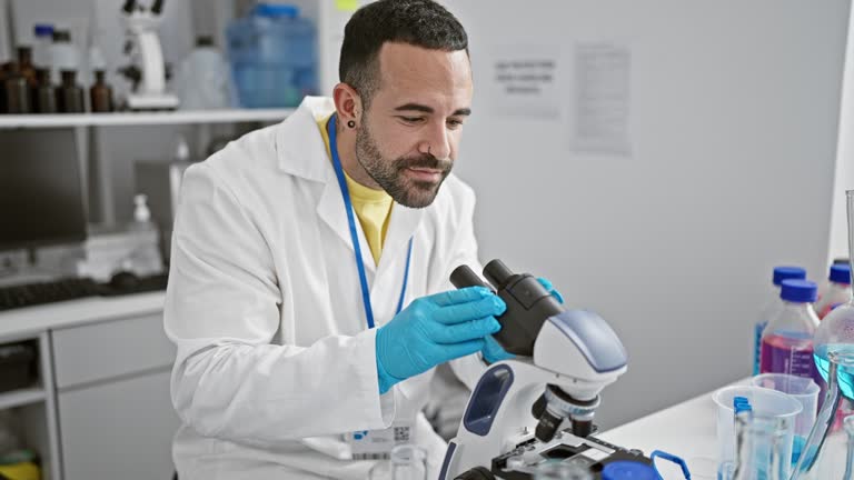 Hispanic male scientist analyzing samples through a microscope in a laboratory environment.