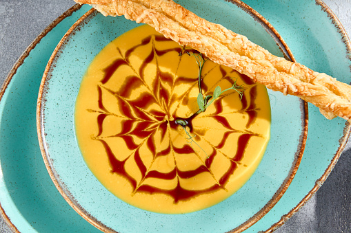 A top view, closeup, and horizontal orientation reveal the delicious details of pumpkin soup with crostini. The gray concrete table serves as a minimalist backdrop.