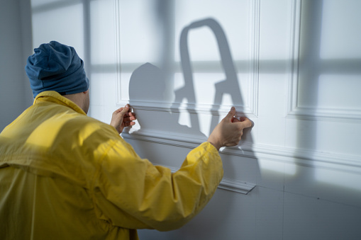 Close-up shot of man crouching and setting moldings on white wall during home renovation