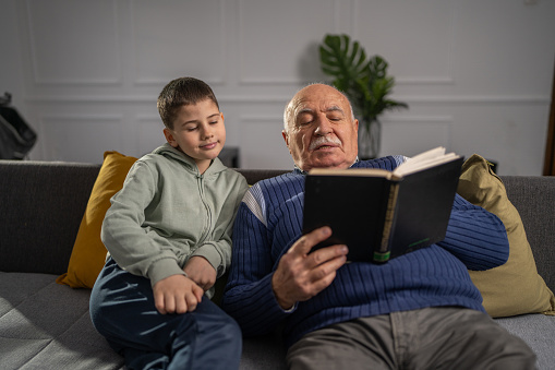 Grandfather and grandson enjoying time together while sitting on sofa and reading a book at home