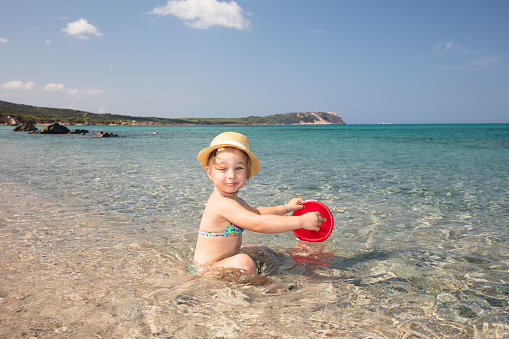 Just outside the town of Santa Teresa Gallura, the transparent and colorful sea amazes any visitor. Here is the magnificent sandy beach of Rena di Mateu, uncrowded even in high tourist season. A little girl is playing with the sand in the shallow waters.