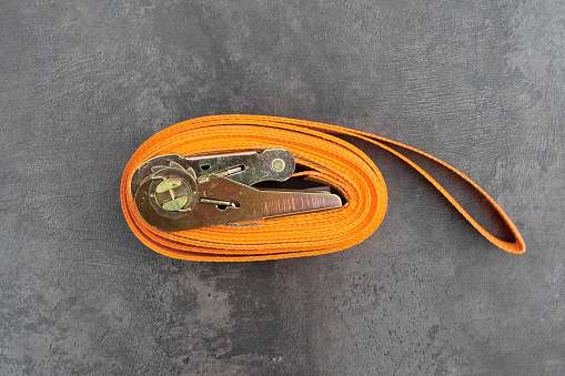 An orange tie-down strap for securing a load, rolled into a roll on a table surface. Securing and transporting cargo.