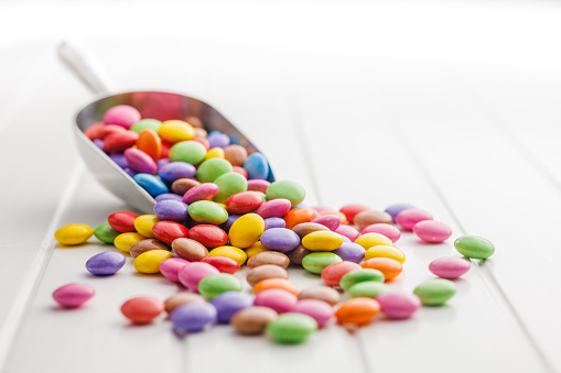 Colorful sweet candies in scoop on the white table.