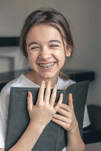 A teenage girl reads a book and smiles, showing her teeth with braces. Orthodontic treatment concept.