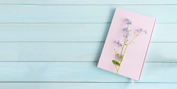 Pink book or notebook with a sprig of forget-me-nots on a light blue wooden background