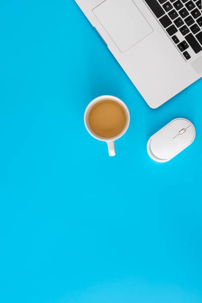 A top view of a well-organized office space featuring a computer, keyboard, mouse, calculator, and a cup of coffee alongside eyeglasses on a dark mat.