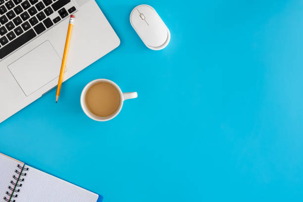 istock Laptop with notebook and cup of coffee on blue background. 1989670167