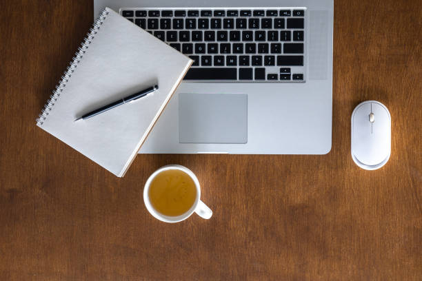 Laptop, cup of tea and notepad on a wooden table, top view. Flat lay office desk.