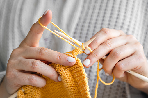 Close-up of female hands knitting yellow wool sweater. The girl goes in for her hobbies. Knitting concept.