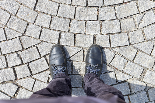 overhead view of the legs of a man standing on a sidewalk made of granite paving stones