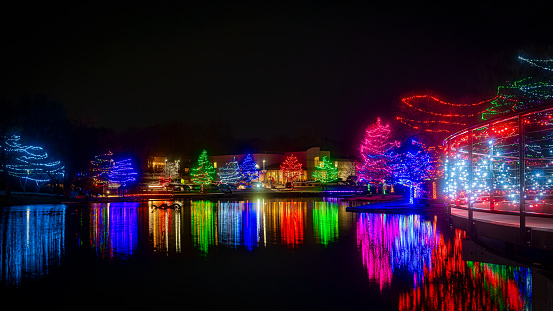 A scenic view of trees illuminated by Christmas lights near a lake at night