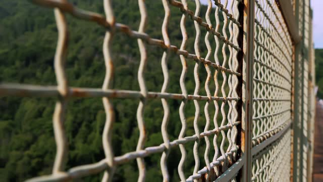 A metal mesh on a bridge, guarding against a precipice, serving as a barrier to prevent suicides, often linked to disappointments, divorces, bankruptcies.