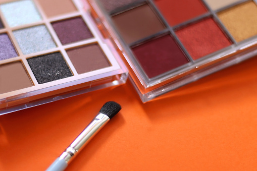 Colorful eyeshadow palettes and make up brush on orange background. Selective focus.