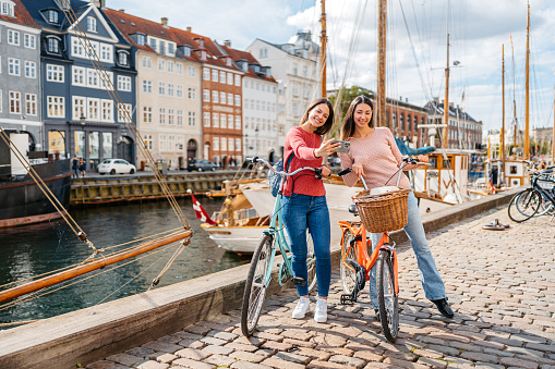 Two female friends with bicycles taking selfies in Nyhavn Canal in Copenhagen in Denmark.