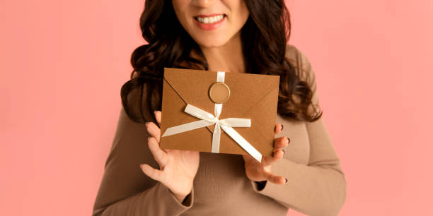 istock Elegant woman holding envelope Gift Certificate in hands on pink background 1989758887