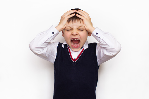 Attention deficit hyperactivity disorder or ADHD and autism concept. Angry, crazy, irritated, upset boy in a school uniform holds his head and screams. Back to school, stress, children's emotions