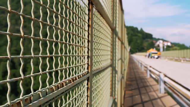 A metal mesh on a bridge, guarding against a precipice, serving as a barrier to prevent suicides, often linked to disappointments, divorces, bankruptcies.