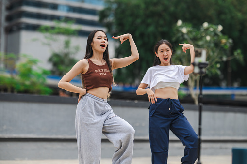 Two young Asian Chinese women using mobile phone for filming their performing dance challenge for social media on the street.